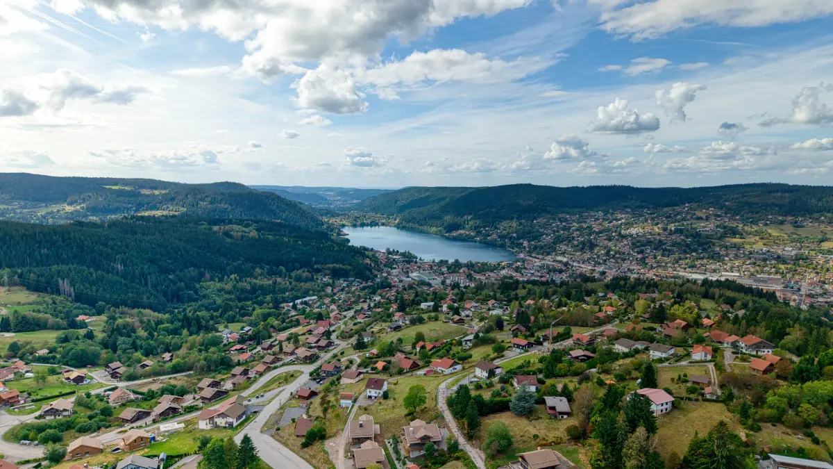 Vue aérienne de Gérardmer et de son lac depuis les hauteurs, chalets et forêt au premier plan