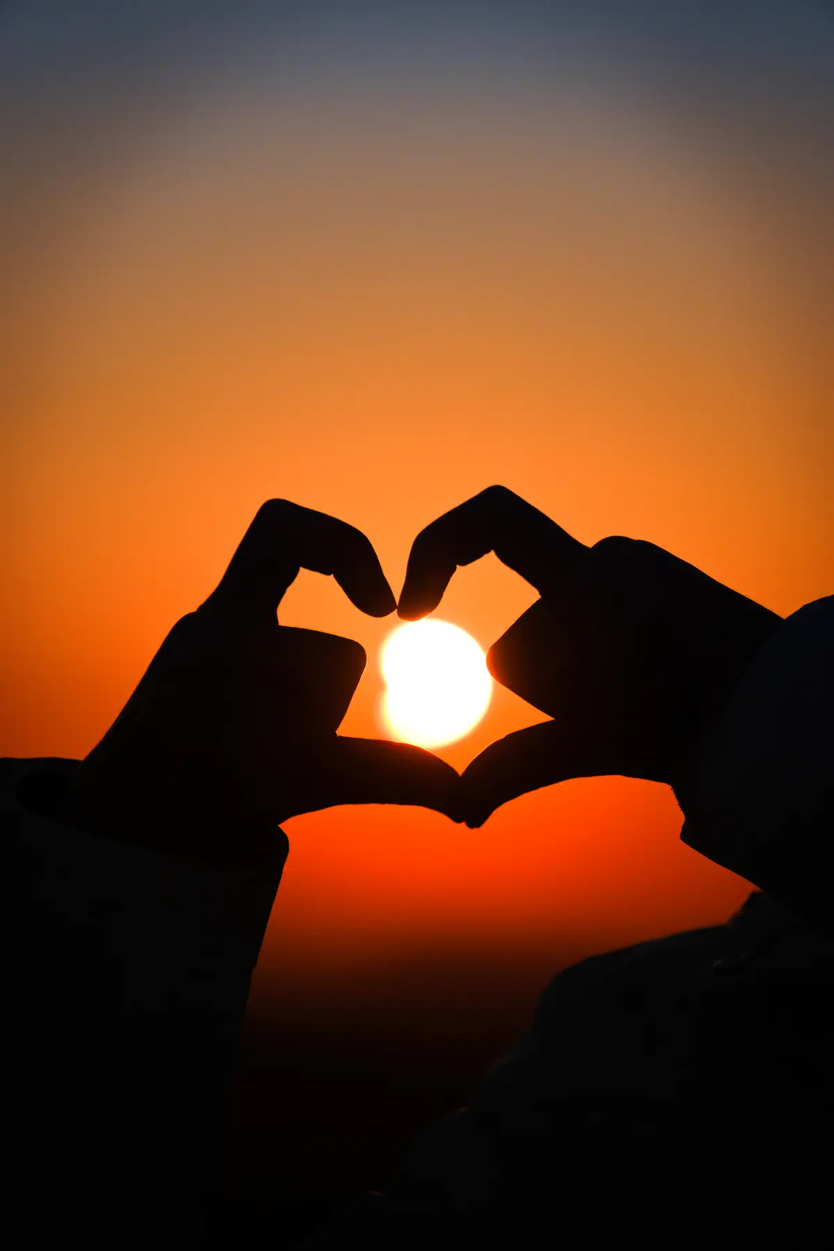 Mains formant un cœur autour du soleil couchant